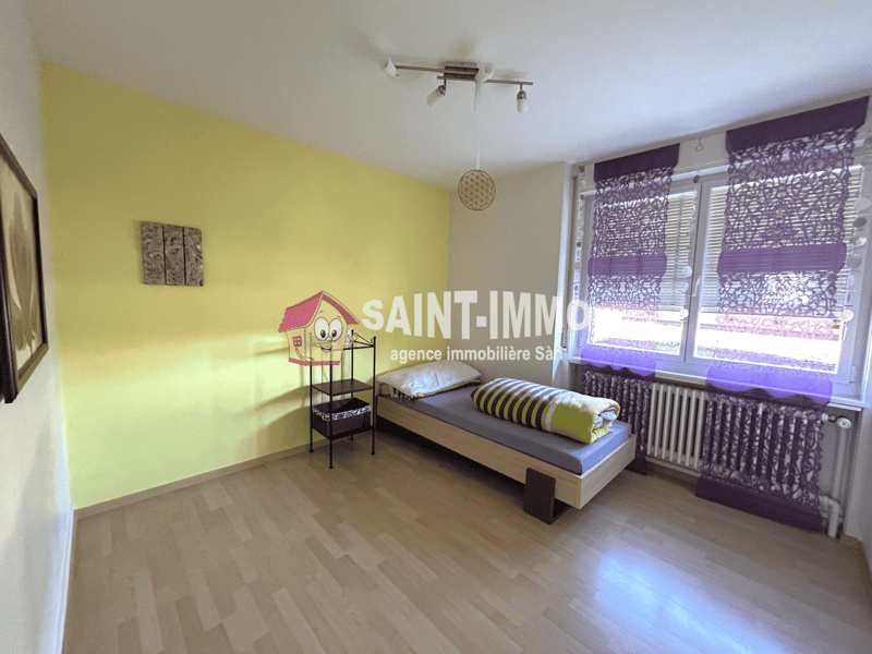 Spacious bedroom with yellow walls, hardwood flooring, a single bed, a shelving unit, and purple patterned curtains covering the window.