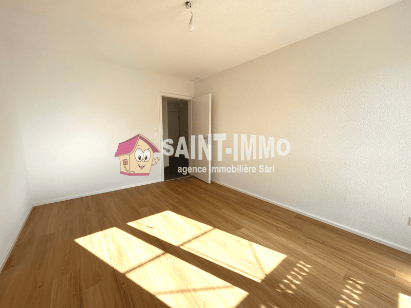 Spacious room with hardwood flooring, white walls, and a single light fixture. The room appears to be empty, providing a clean and minimalist look.