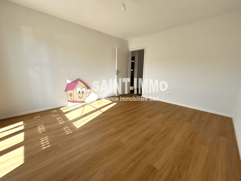 Spacious room with hardwood flooring, white walls, and a bright, airy atmosphere due to the large windows allowing natural light to enter the space.