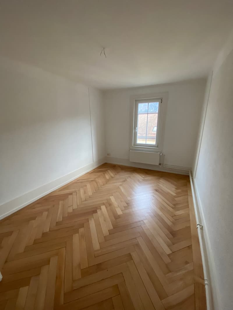 Empty room, wooden parquet flooring, white walls, window with white frame, heating element