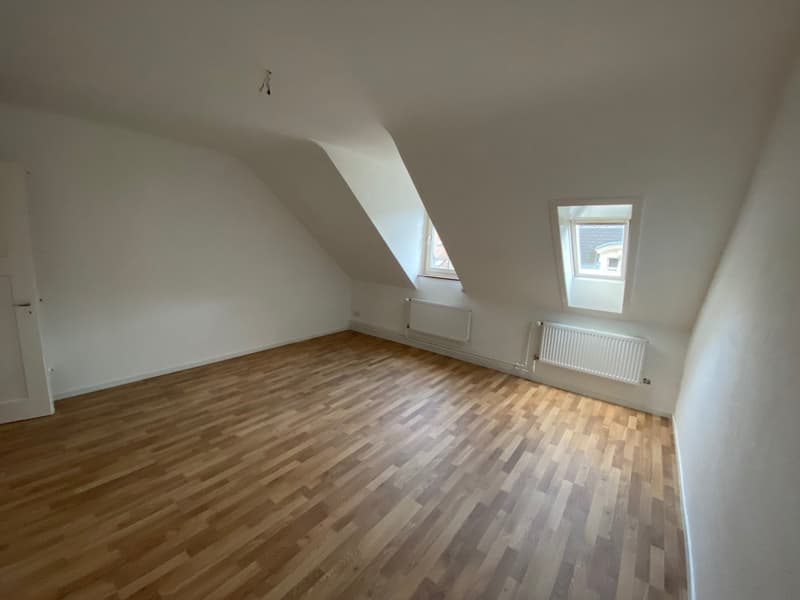 empty room with wooden floors, two attic windows, sloped ceiling, radiators