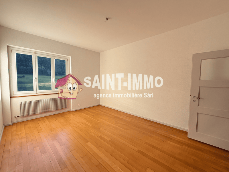 Empty room with wooden floors, white walls, double window, closed door, and heating radiator