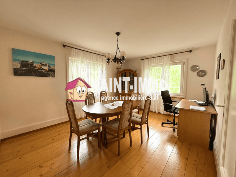 Dining room with wooden floor, round table, chairs, chandelier, desk, computer, office chair, windows with curtains, picture frames, wooden cabinet