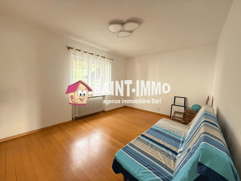 Empty room with wooden floor, white walls, large window with white curtains, ceiling lights, white radiator, sofa with blue and white striped cover