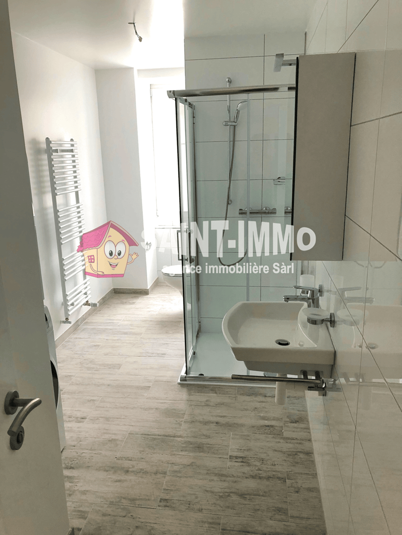Modern bathroom with a glass shower enclosure, white sink, and a white toilet. The floor is tiled, and there is a towel rack on the wall.