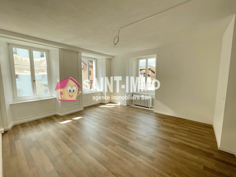 Empty room with white walls, wooden floor, and three windows. There is a radiator on the wall.