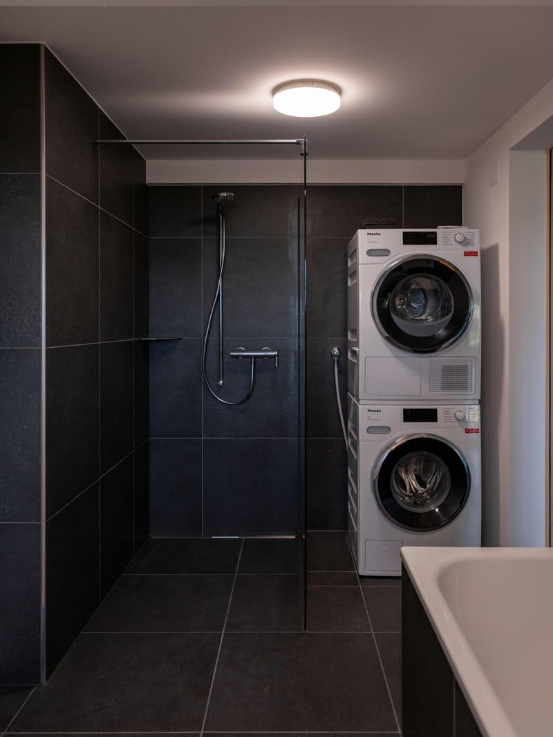 modern bathroom with tiled walls, walk-in shower, bath, stacked washer and dryer, and a ceiling light