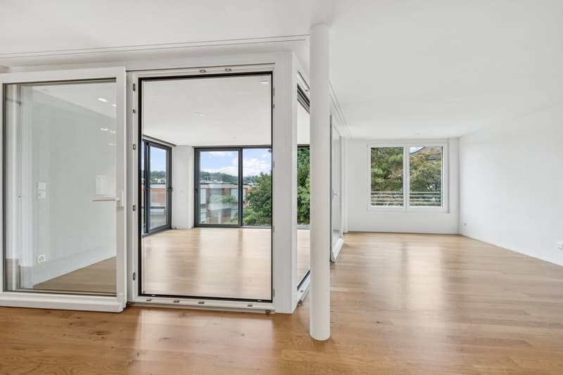 Spacious open-plan living area with large windows and sliding glass doors leading to a balcony or terrace, hardwood floors, and a bright, airy atmosphere.