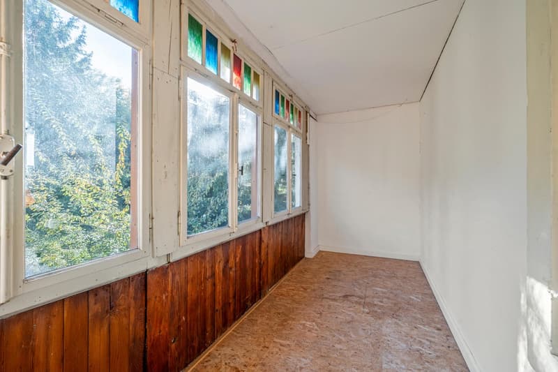 balcony with large windows, wooden walls, brown tiled floor, view of greenery outside