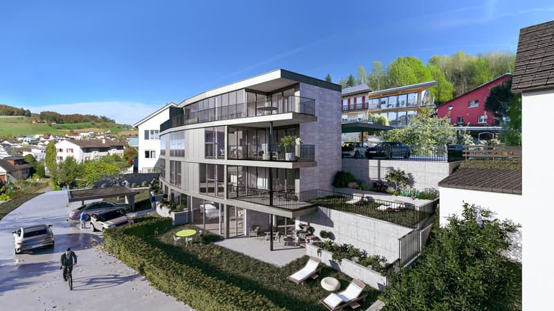 A modern multistory building with balconies, glass windows, and a sloped roof. The building is surrounded by a lush landscape with various plants and trees. There are a few cars parked in front of the building and also a car driving on the road.