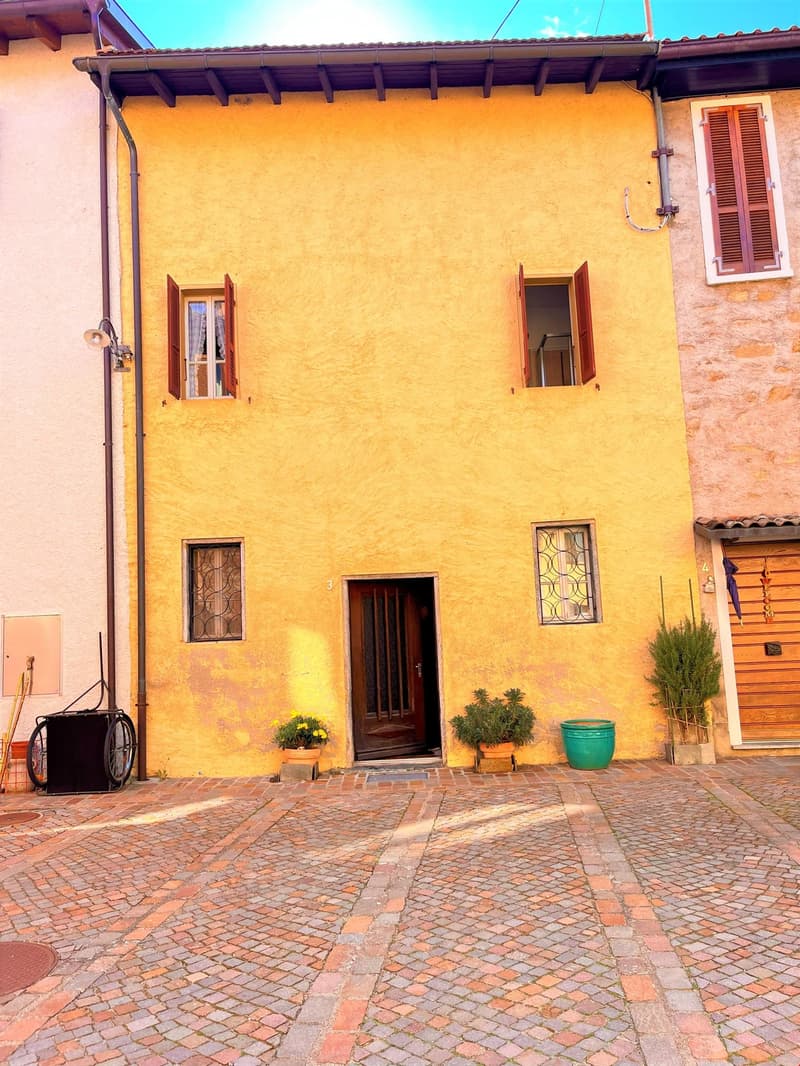 yellow brick building, wooden door, three windows, brick paved courtyard, plants