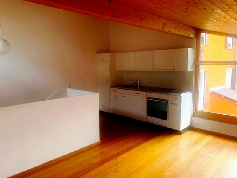 Open plan kitchen with wooden floors, white cabinets, built-in appliances and a large window offering a view of an adjacent building.