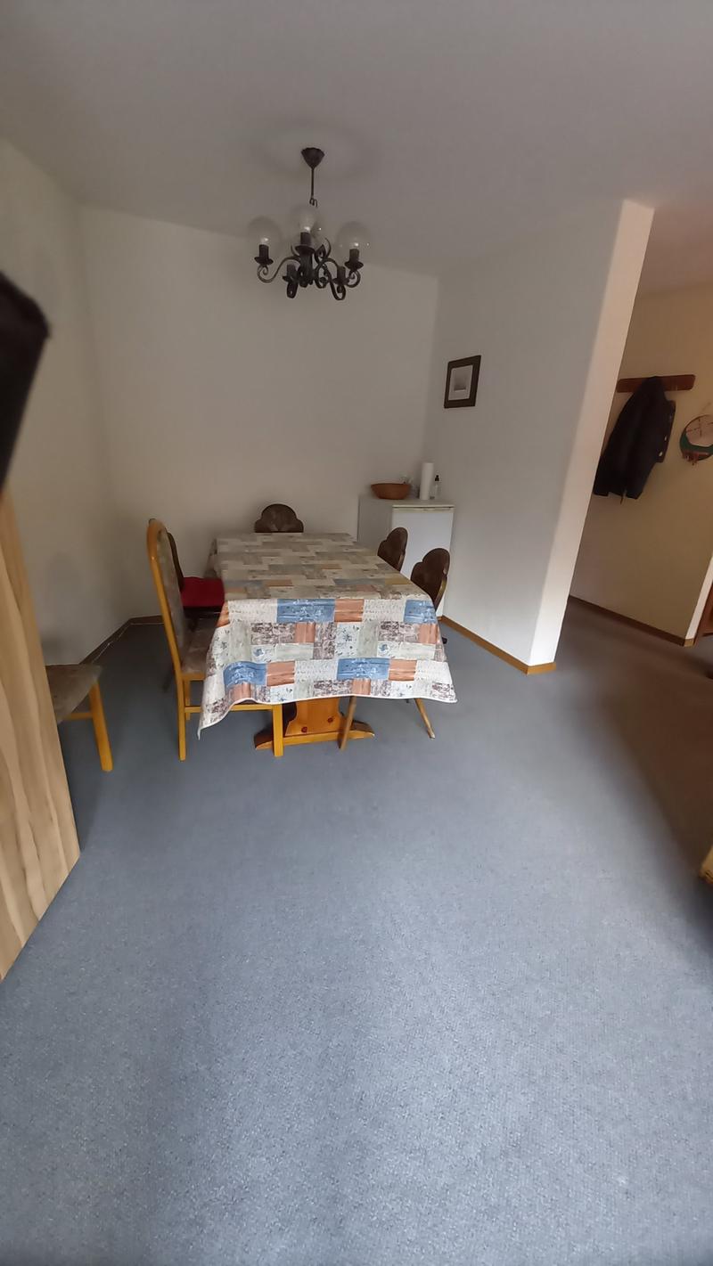Dining room with table, chairs, chandelier, white walls, white refrigerator, picture frame, bowl, and coat hanging on the wall.