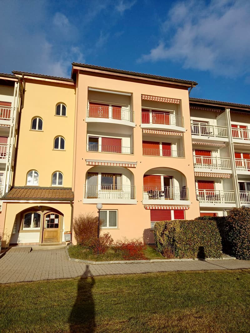 yellow apartment building with many balconies, red shutters, red roof, multiple floors, shrubs in front
