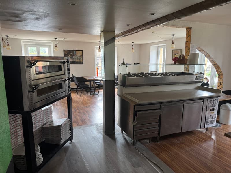 Commercial-grade kitchen with stainless steel appliances, including a double oven and a large refrigerated prep counter. The space also features hardwood floors and exposed ceiling beams.