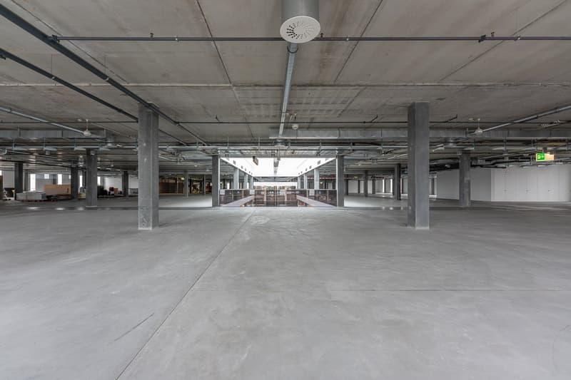 large open space, exposed concrete ceiling and columns, concrete floor, windows, no interior furnishings