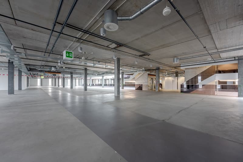 Parking lot, gray concrete floor, multiple pillars, illuminated by ceiling lights, exit sign on the ceiling, no vehicles present