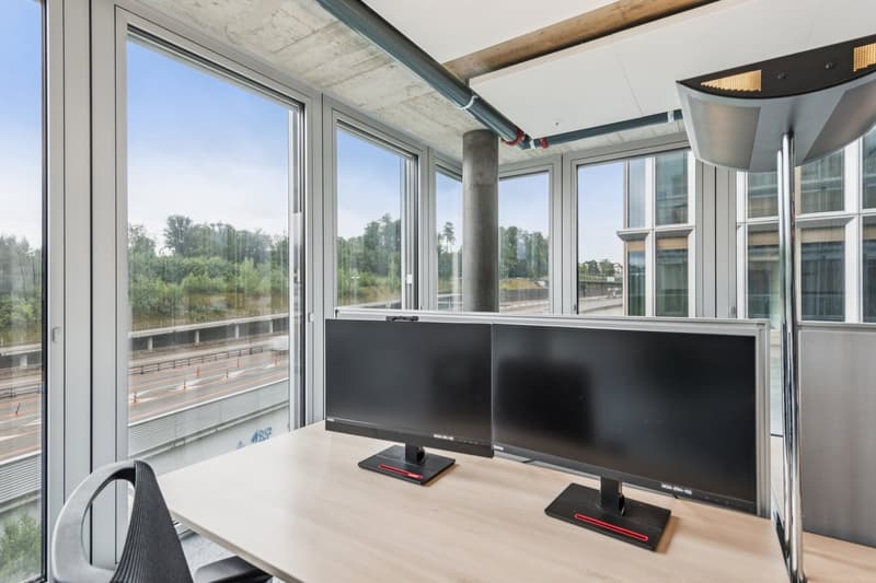 Wooden desk, two monitors, chair, large windows with a view of the city