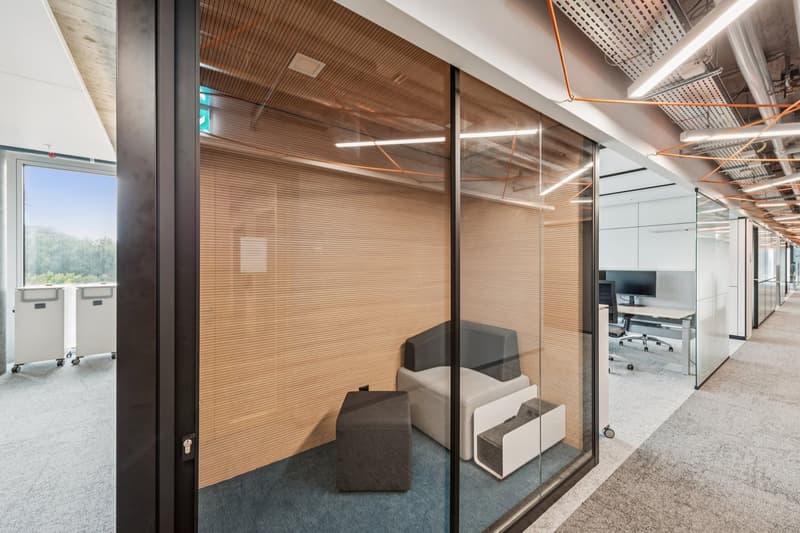 open office with wooden partitions, glass walls, comfortable seating, computer desk, filing cabinets, and a view of trees outside