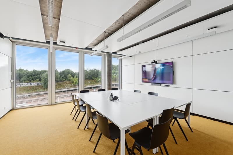 Empty conference room with large windows, long table, black chairs, mounted monitor