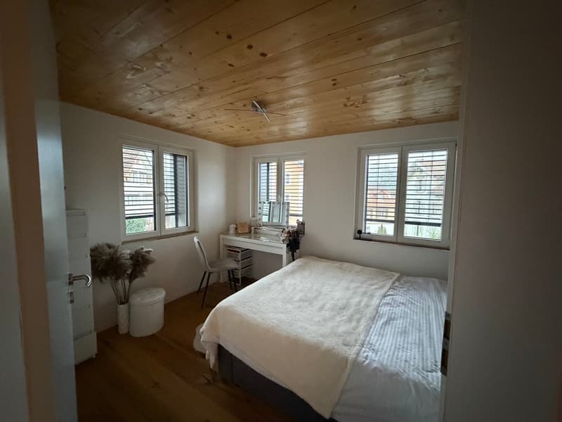 large bed, desk, chair, plants, wooden floor, wooden ceiling, three windows