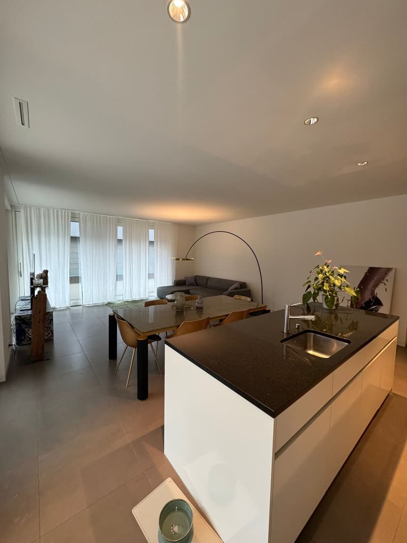 modern open-plan kitchen with black marble countertop, white cabinets, dining table, and large windows with curtains