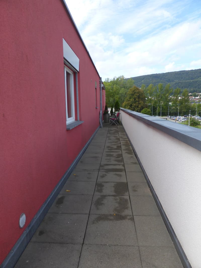 A balcony with gray tiles, red walls, a chair, and a plant. A view of the mountains.