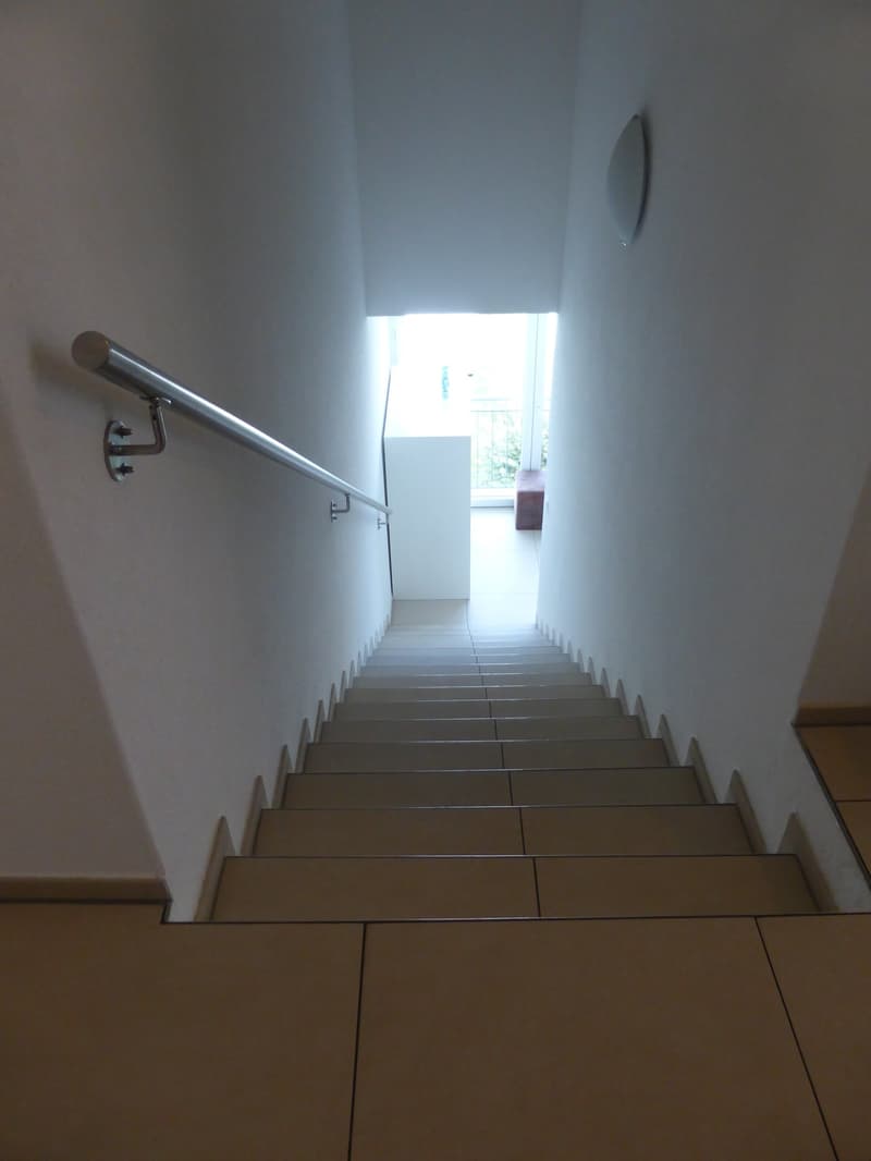 modern staircase with tiled steps and metal handrail, white walls, tiled flooring, small bench at the top, wooden panelling on the side wall