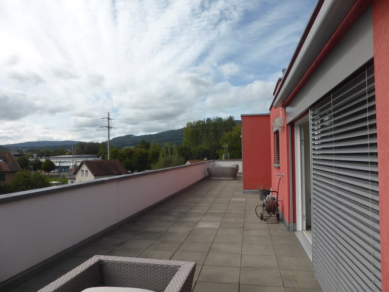 tiled terrace with railing, outdoor seating, clear sky with clouds, distant houses, greenery