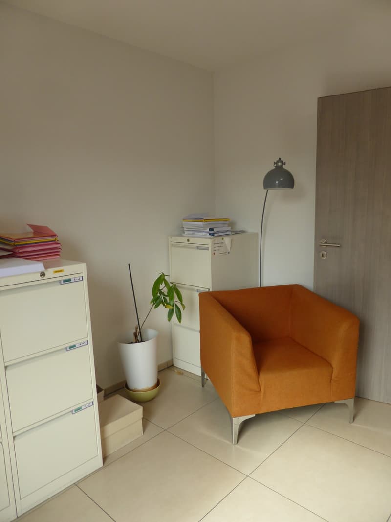 Office room with white walls, beige tiles, single orange chair, lamp, plant, file cabinets, filing cabinet, door