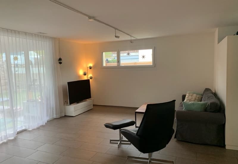 Living room with white walls, tile floor, couch, coffee table, television, ottoman, two black chairs