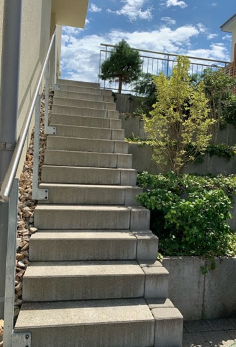 Concrete stairs with a metal handrail, small planted area on the side, garden with plants and a fence