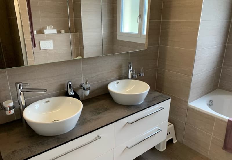 modern bathroom with two sinks, bathtub, white cabinets, and tiled walls