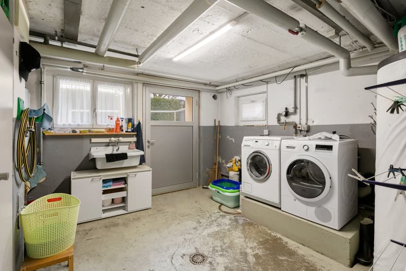 Laundry room with washing machine, dishwasher, sink, cabinets, shelves, drying rack, brooms, storage baskets, and cleaning products.