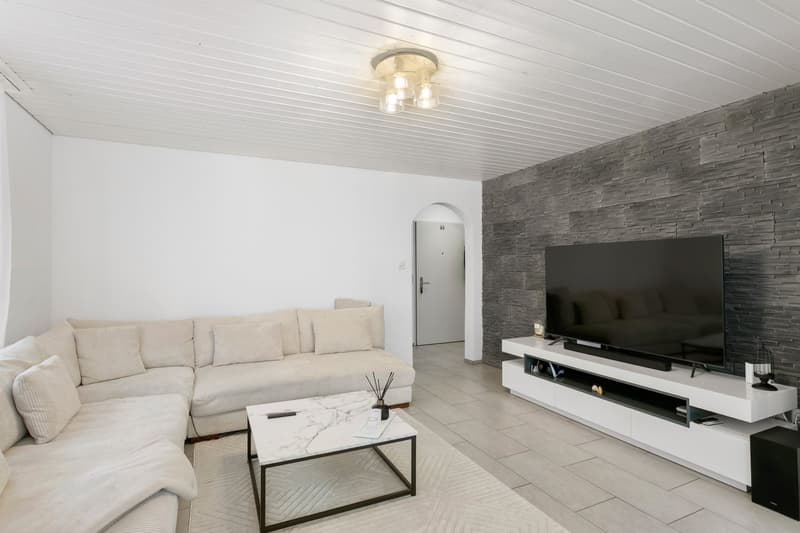 L-shaped sofa, TV, coffee table, tiled floor, white and grey walls, ceiling lights