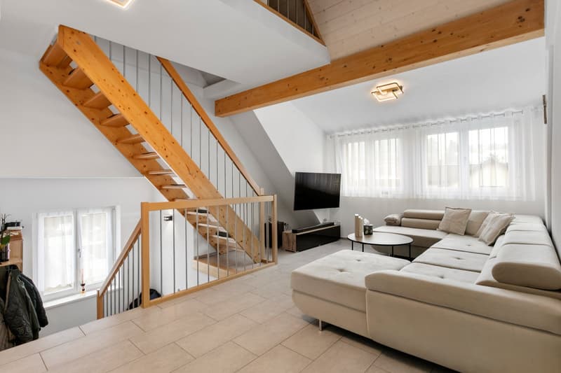 Stairs leading to raised floor, lounge with L-shaped couch, TV, glass table, wooden beams