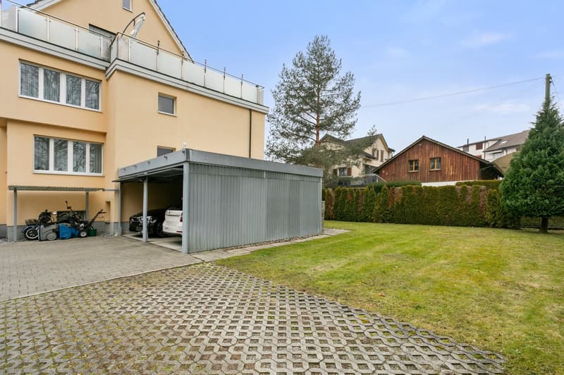 yellow facade house, 2 garage doors, 2 cars in garage, hedge, lawn, trees