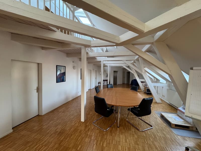 wooden floor, exposed beams, round wooden table, black chairs, picture on the wall, ladder leading to the upper floor, door at the left side, radiator on the right side