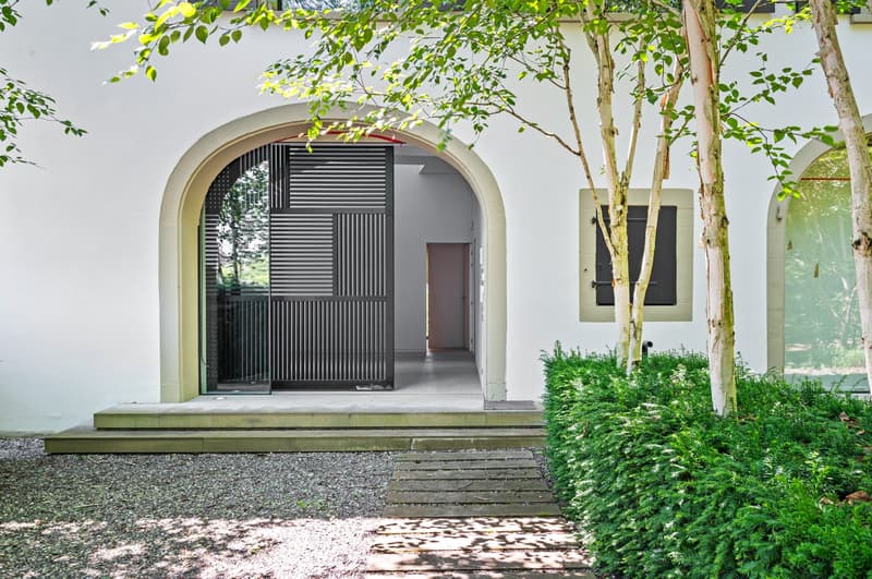 white building, arched entrance, paved path, gravel area, greenery