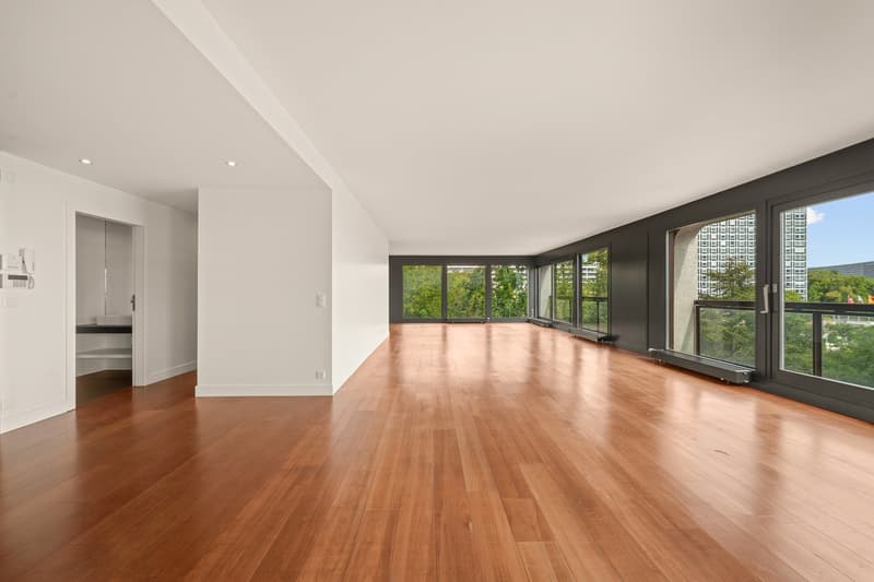 large room with wooden floors, white walls, modern doors, sliding glass windows with balcony, open to the view of trees