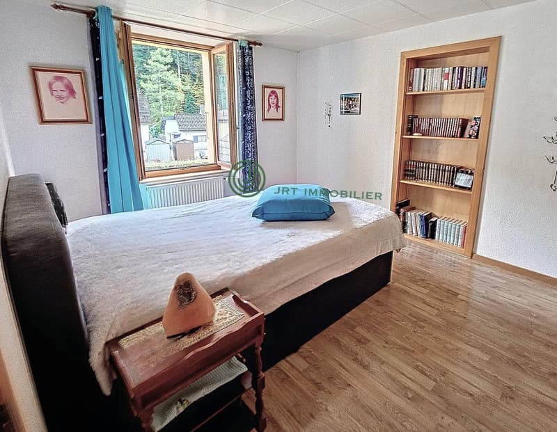 Bedroom with bed, nightstand, bookshelf, window with curtains, picture frames, radiator, and a view of the outside.