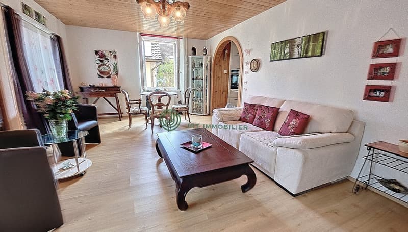 living room with white couch, wooden coffee table, glass table, wooden chairs, wooden desk, flower vase, picture frames, chandelier