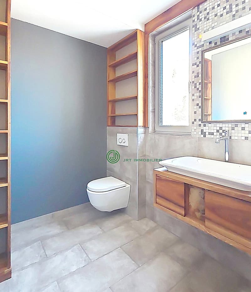 small bathroom with white tiles, wooden shelves, a window, a white toilet, sink, and mirror