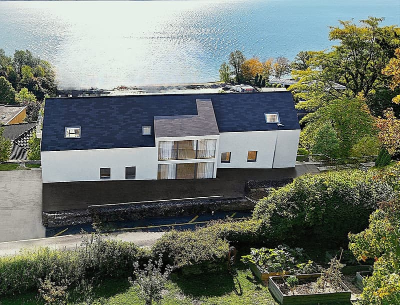 Modern house with a view of the sea, white exterior, black roof, large windows, garden, parking area