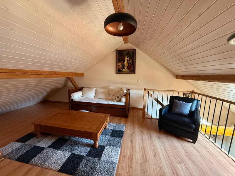 A wooden floor, white ceiling, a sofa, a coffee table, a rug, a wall painting, a balcony, and a wooden staircase.