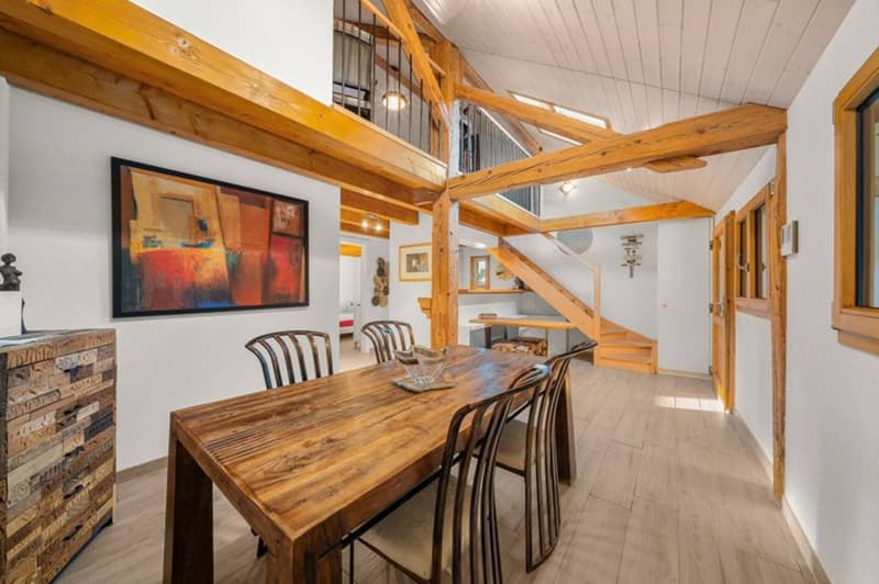 dining room, wooden table, 6 chairs, white walls, wooden beams, staircase, painting on wall