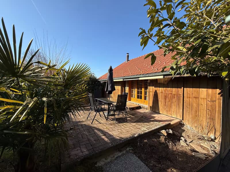 Wooden house with red roof, outdoor seating area, brick patio, palm trees, garden, outdoor table and chairs
