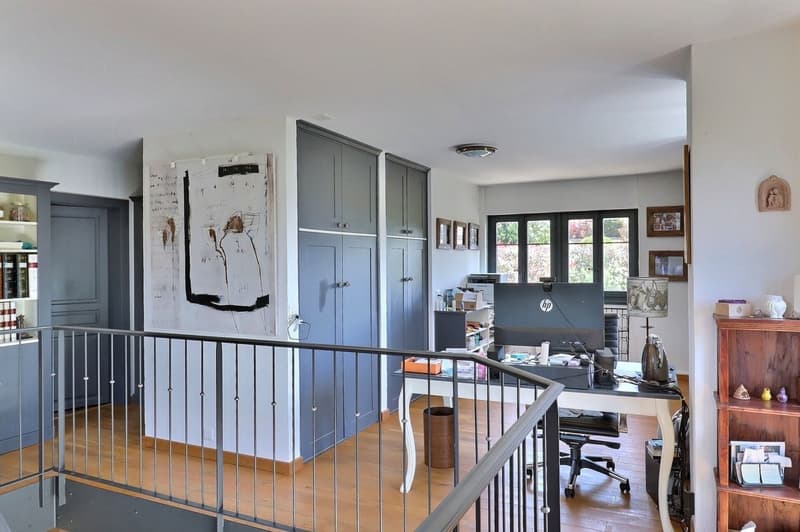 Desk, office chair, monitor, wooden flooring, cabinets, shelves, trash can, iron, picture frames, shelves with books and figurines