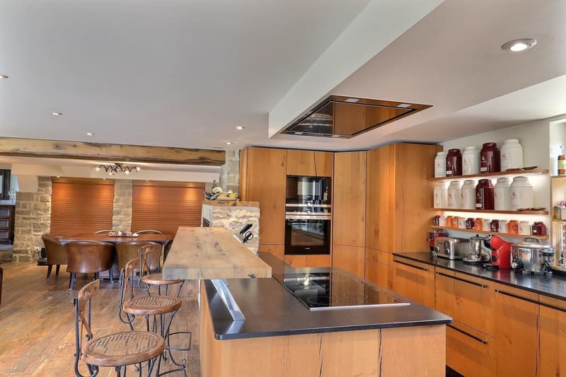 Kitchen with granite counter tops, wooden cabinets, breakfast nook with stools, integrated oven and dishwasher, central island, hardwood floors, gas stovetop, wooden bar.