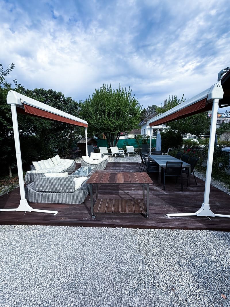 Decked patio with table, chairs, sofas, and white canopies, white pebble floor